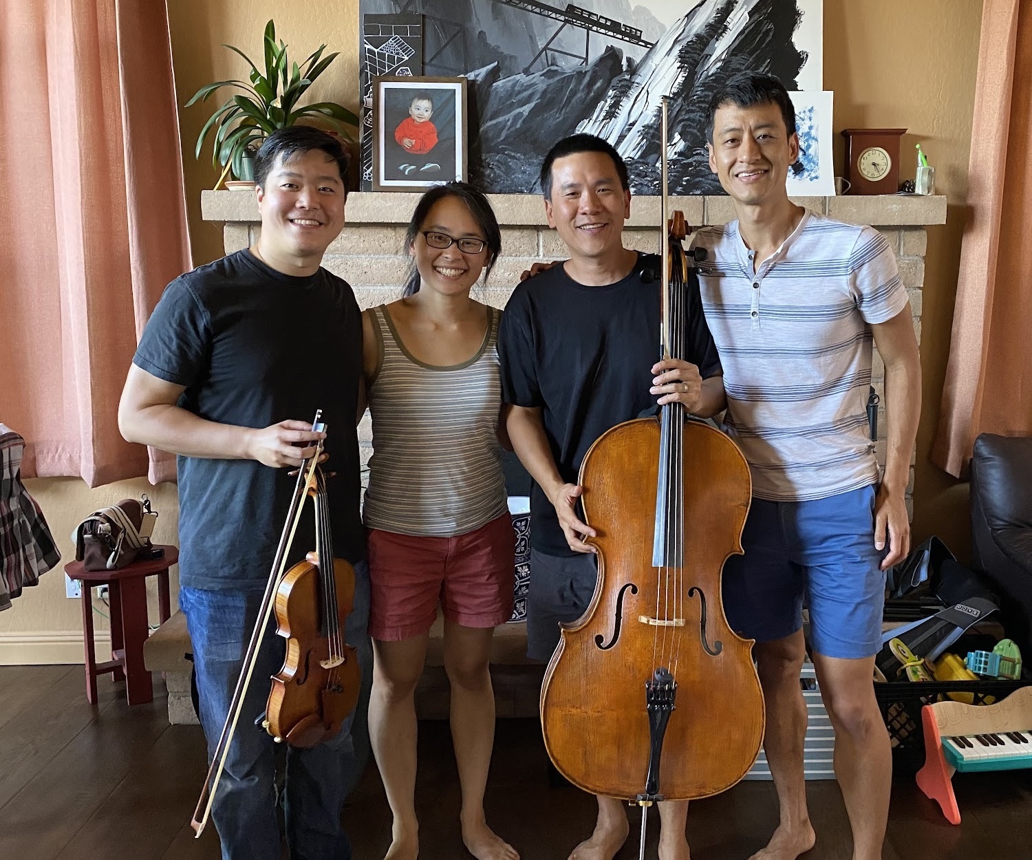 Four musicians standing together in a living room with a violin and cello